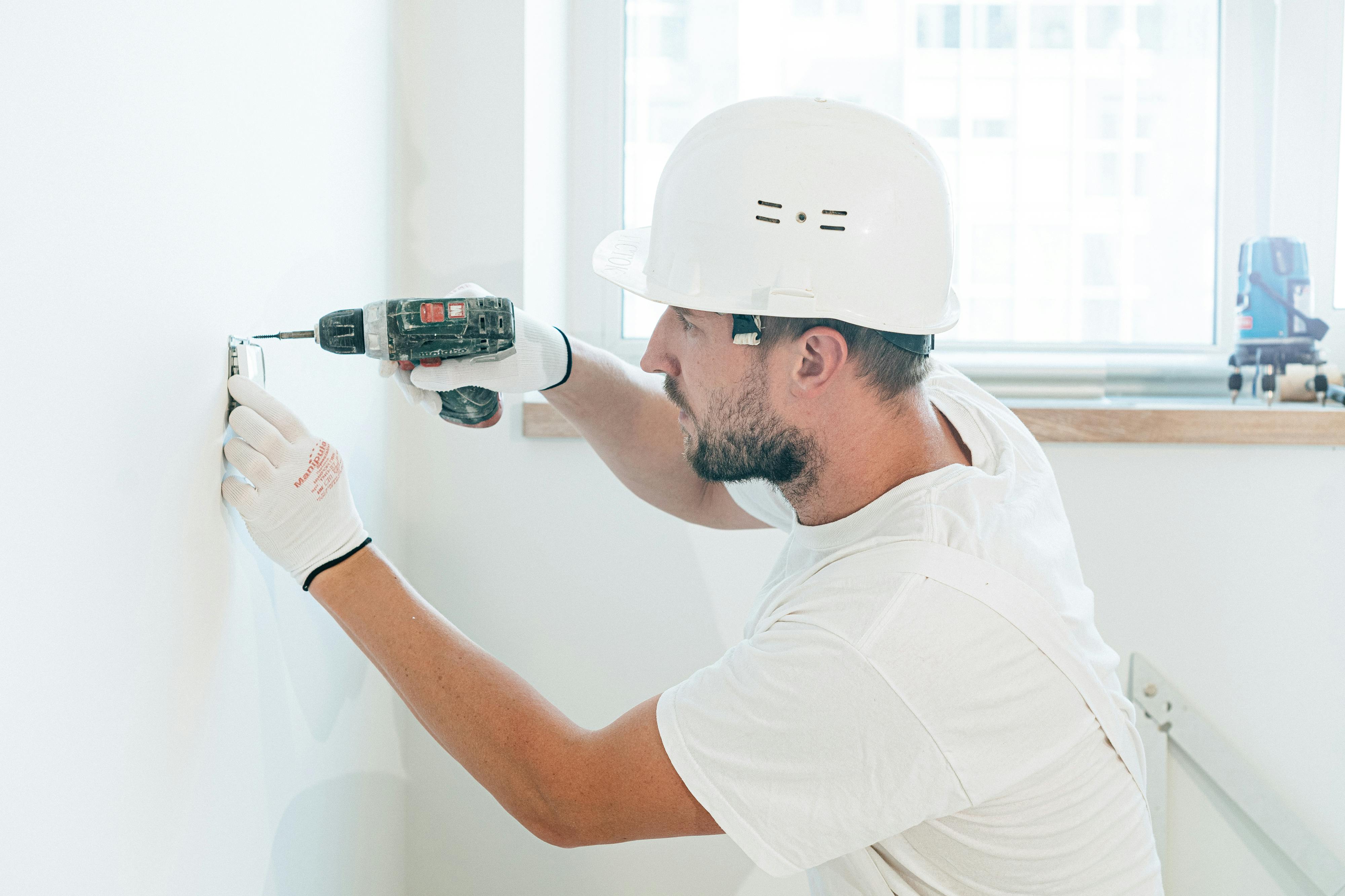 Professional construction worker using power drill on interior wall