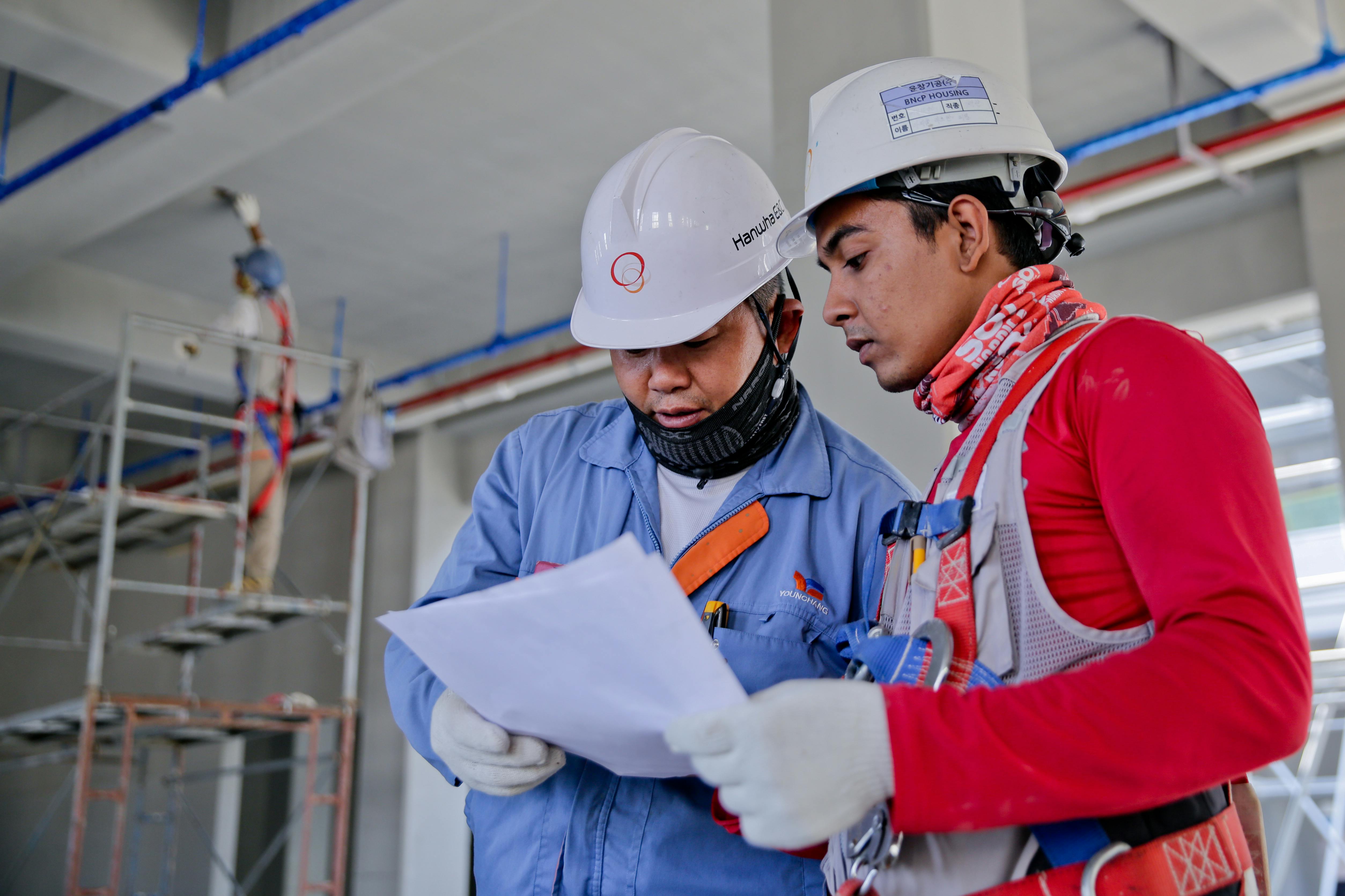 Construction team members in hard hats reviewing blueprints and collaborating on site